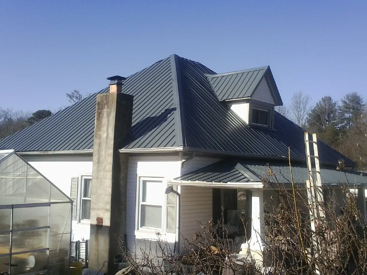 Dark blue standing seam metal roof on a white farmhouse with dormer — Slate & Tile Roof Repair by Roofing Brothers in Channelview