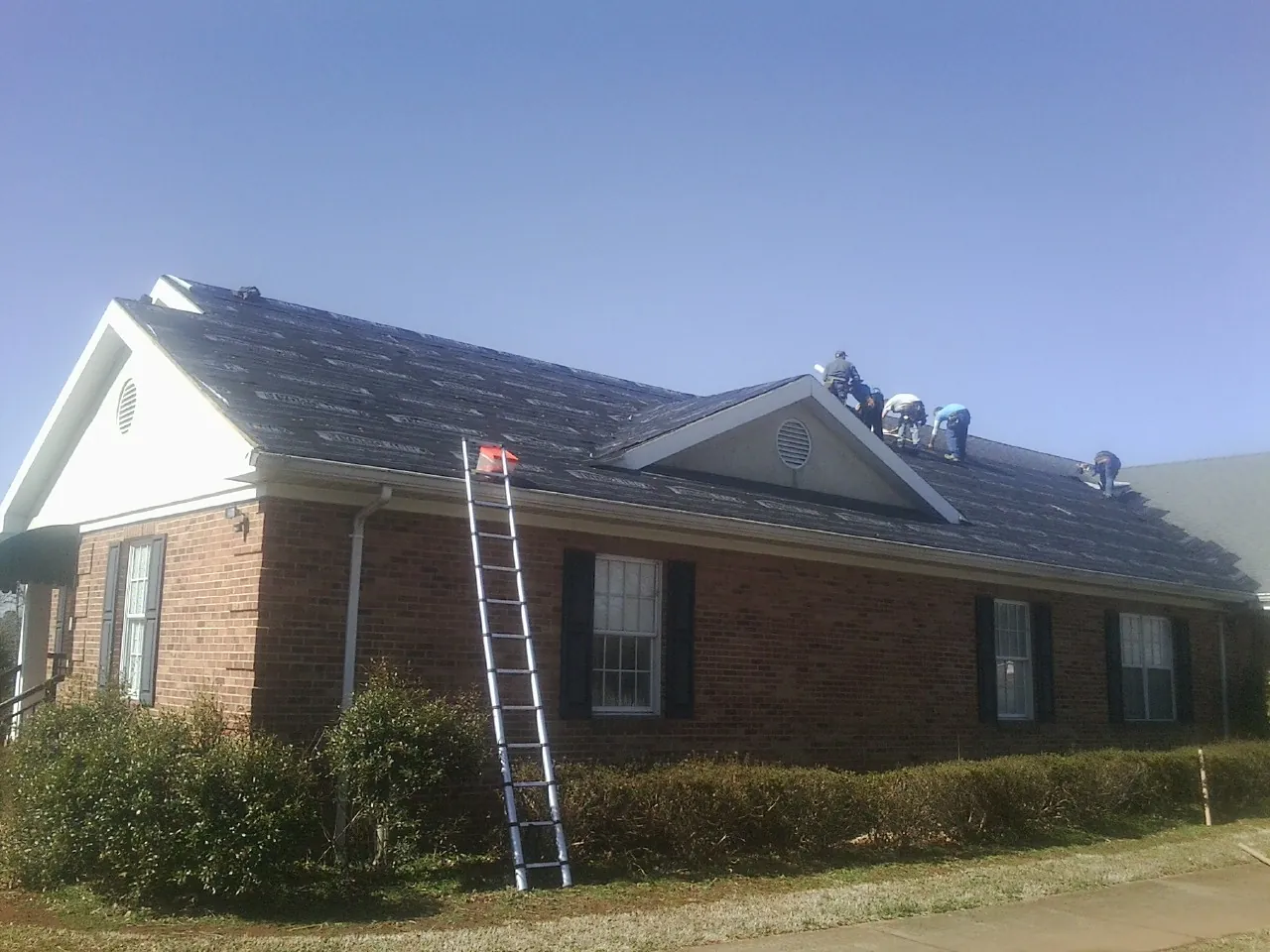 Crew tearing shingles off a brick ranch roof with a ladder set — Emergency Roof Repair work by our crew in Channelview