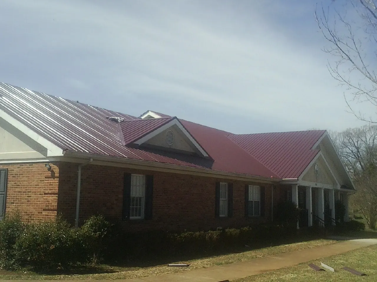 Red metal roof with gabled entries on a long brick building, from a Hail Damage Roof Repair job in Channelview