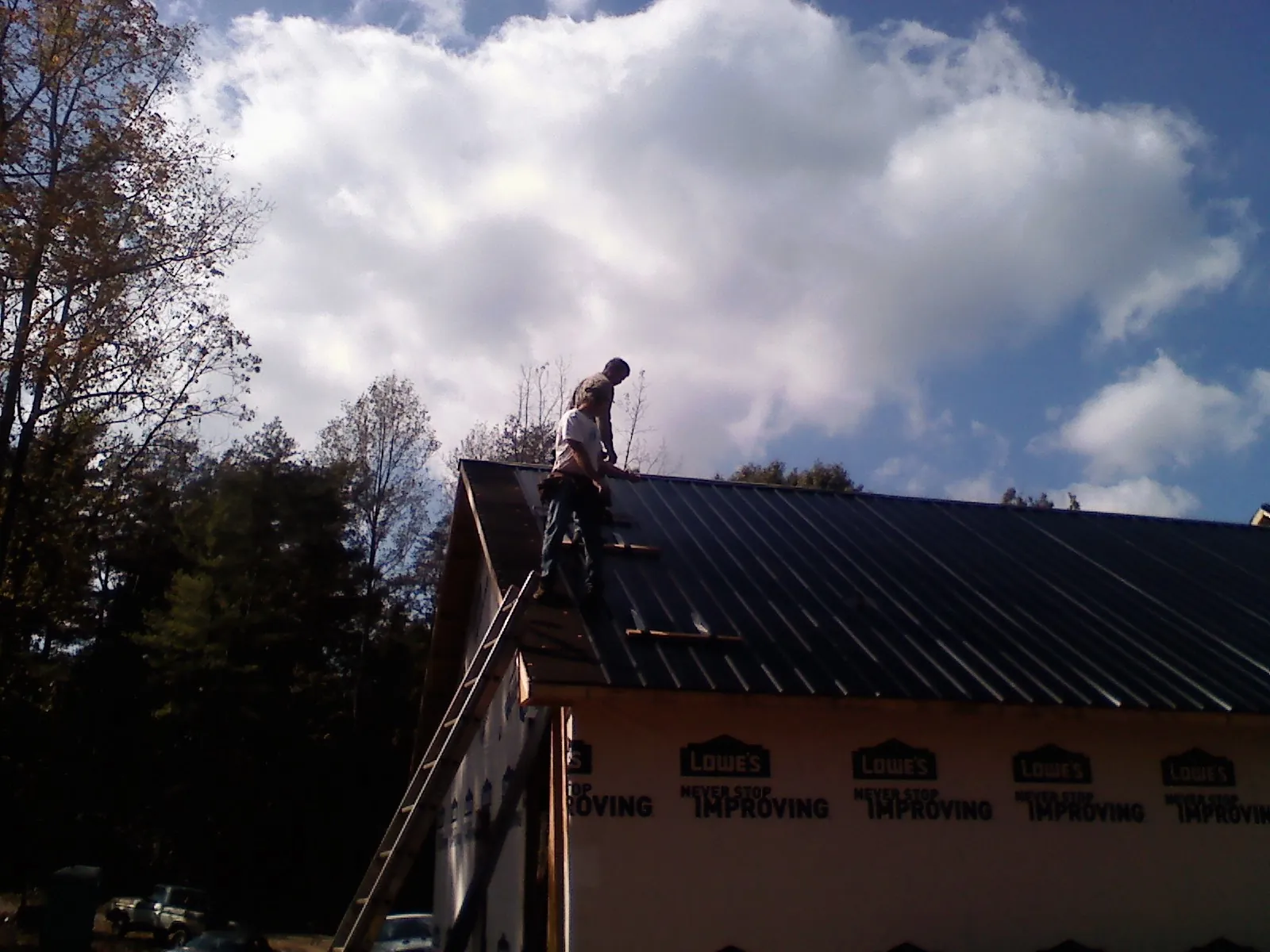Roofer fastening dark metal panels high against a cloudy sky, from a Roof Inspection job in Channelview