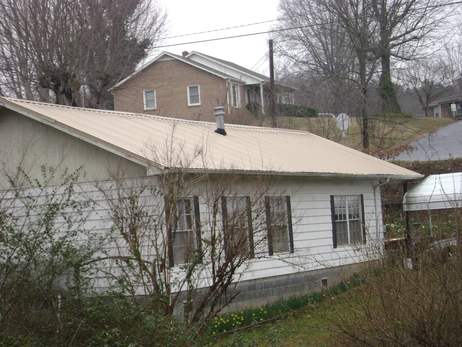 Tan metal roof on a white sided house set into a hillside — Commercial Roofing by Roofing Brothers in Channelview